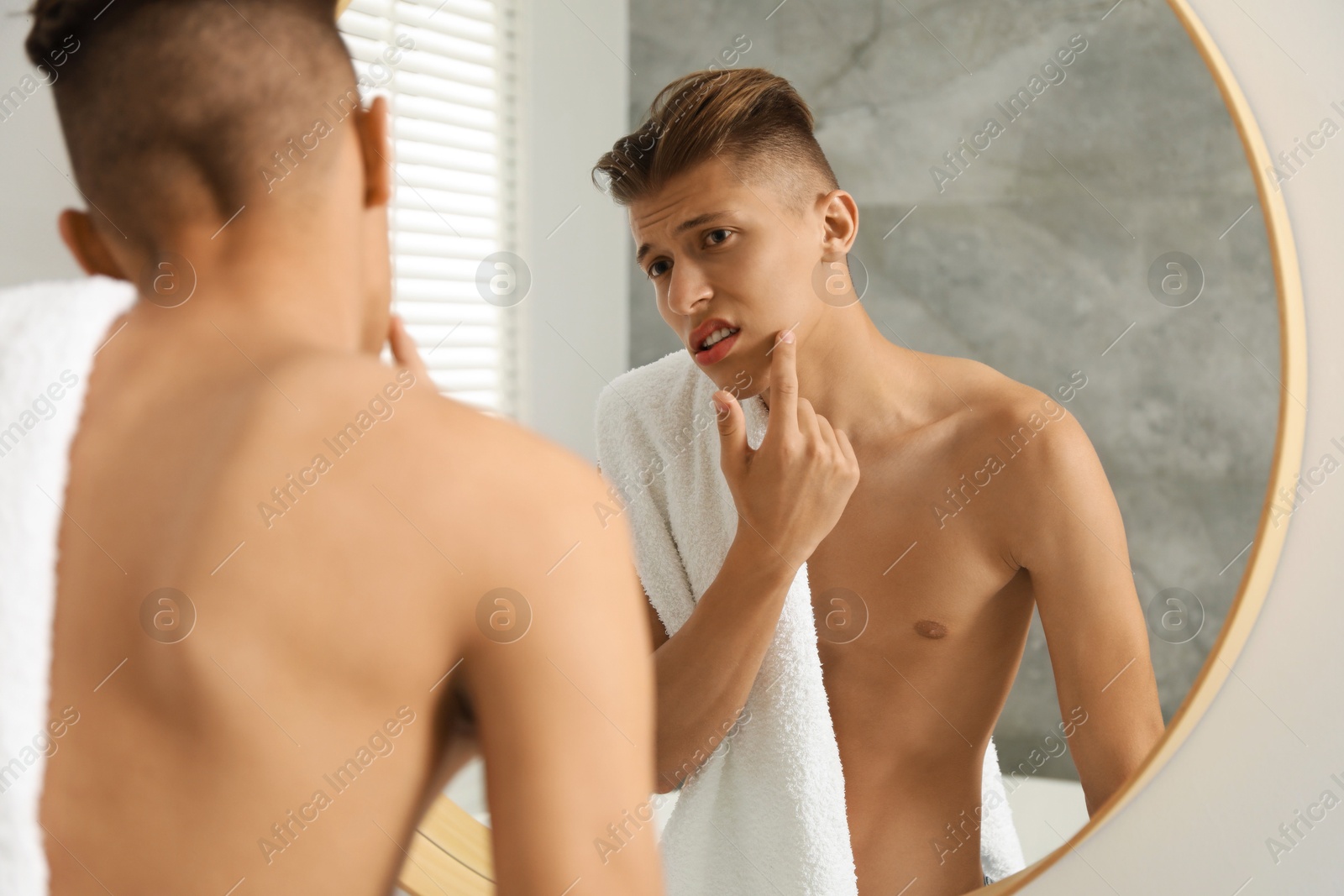 Photo of Man with towel touching his face near mirror in bathroom