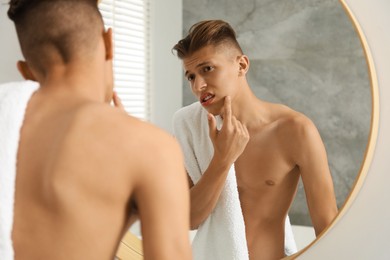 Man with towel touching his face near mirror in bathroom