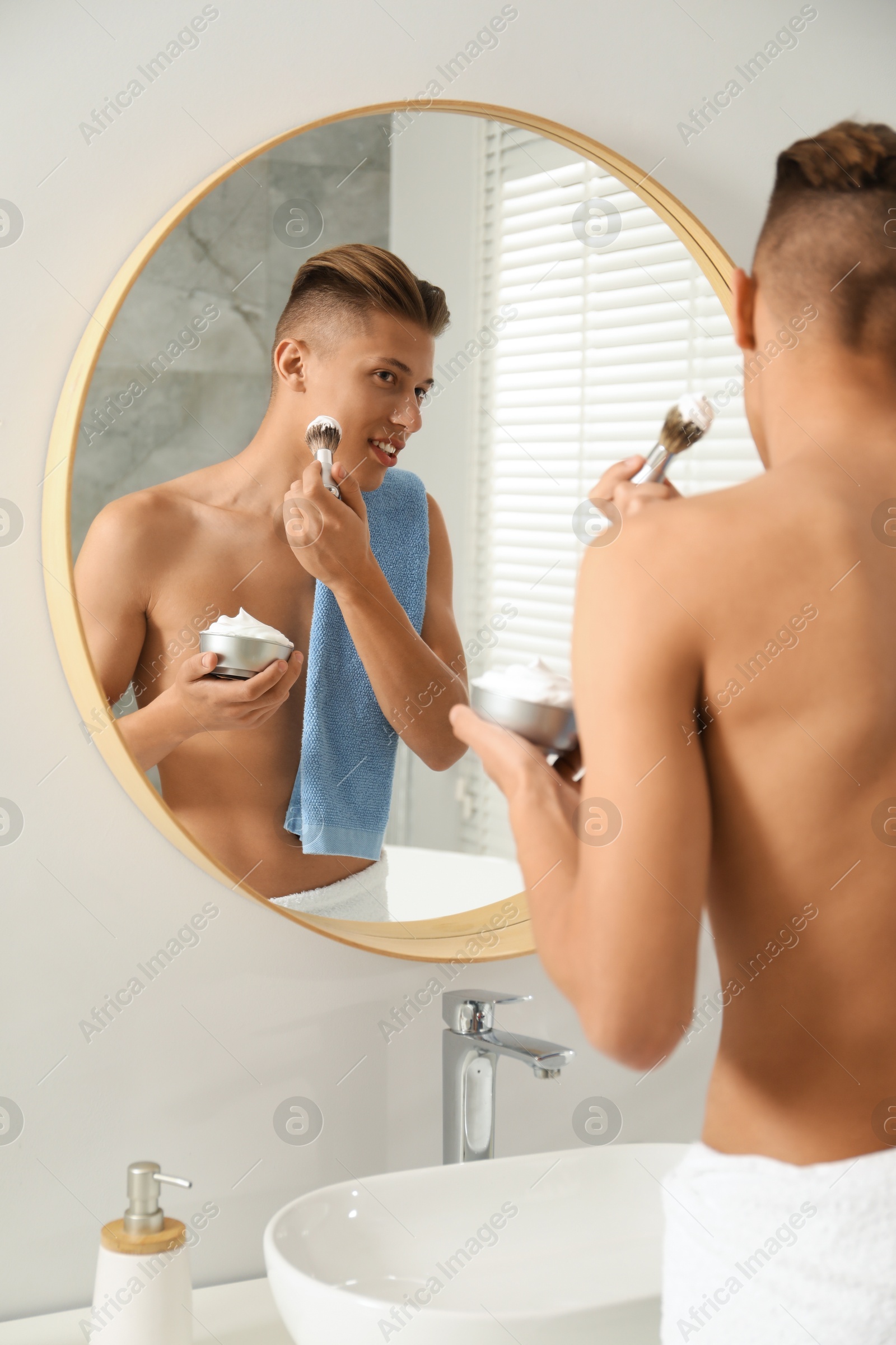 Photo of Handsome man applying shaving foam near mirror in bathroom