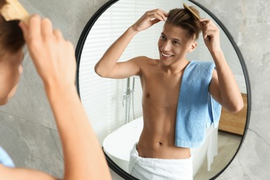 Handsome man brushing his hair near mirror in bathroom