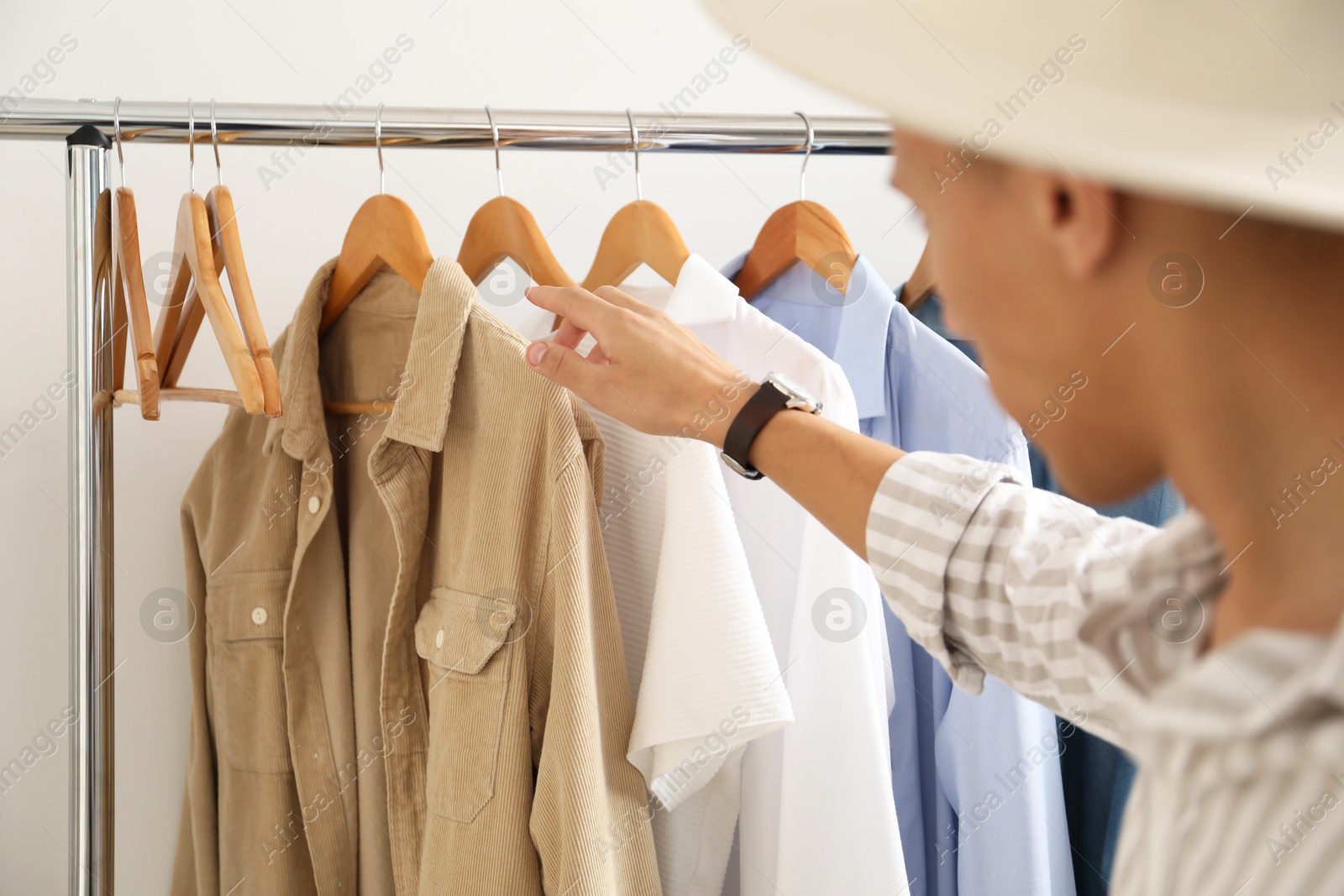 Photo of Man in hat choosing clothes near rack indoors