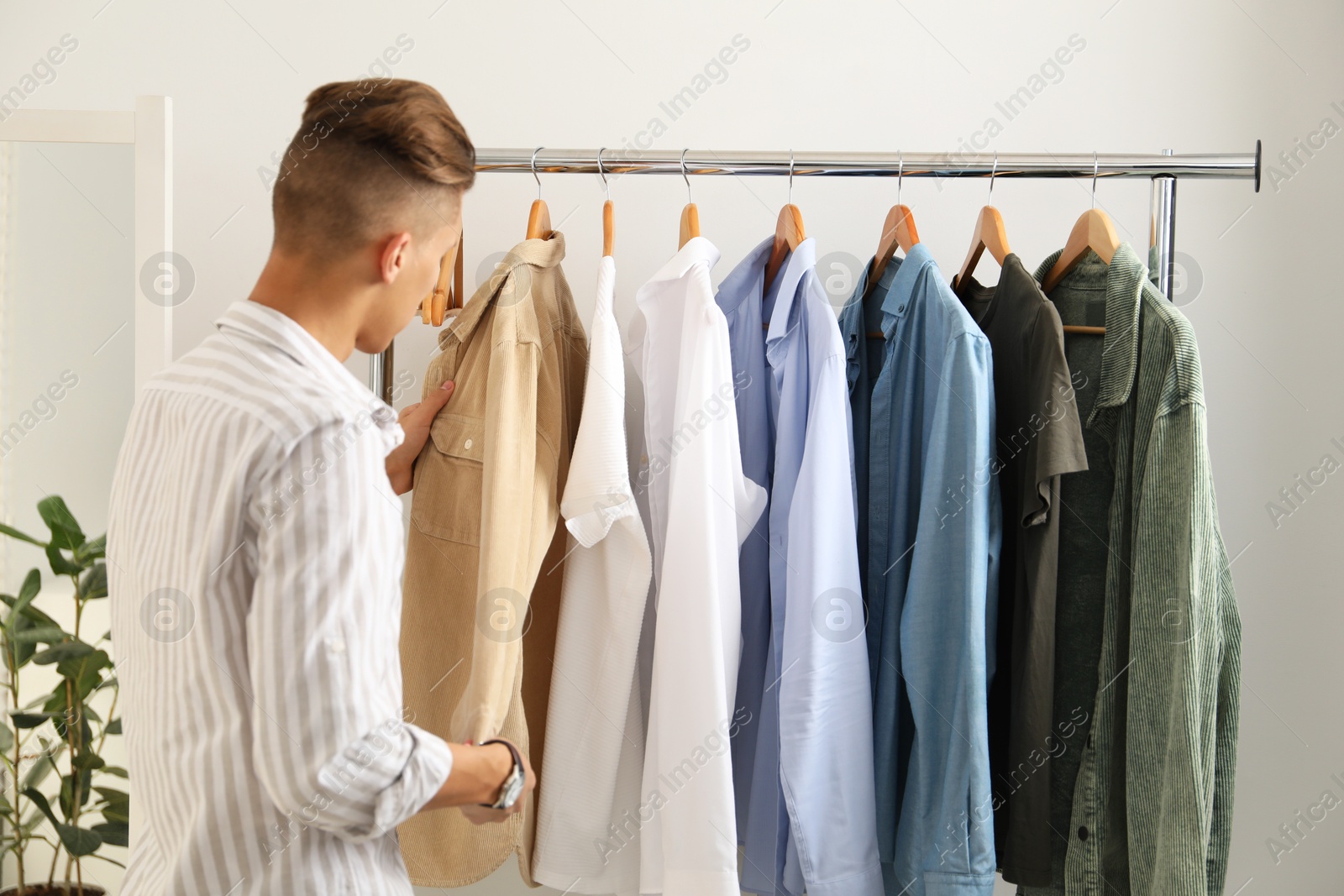 Photo of Man in shirt choosing clothes near rack indoors