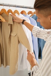 Man in shirt choosing clothes near rack indoors