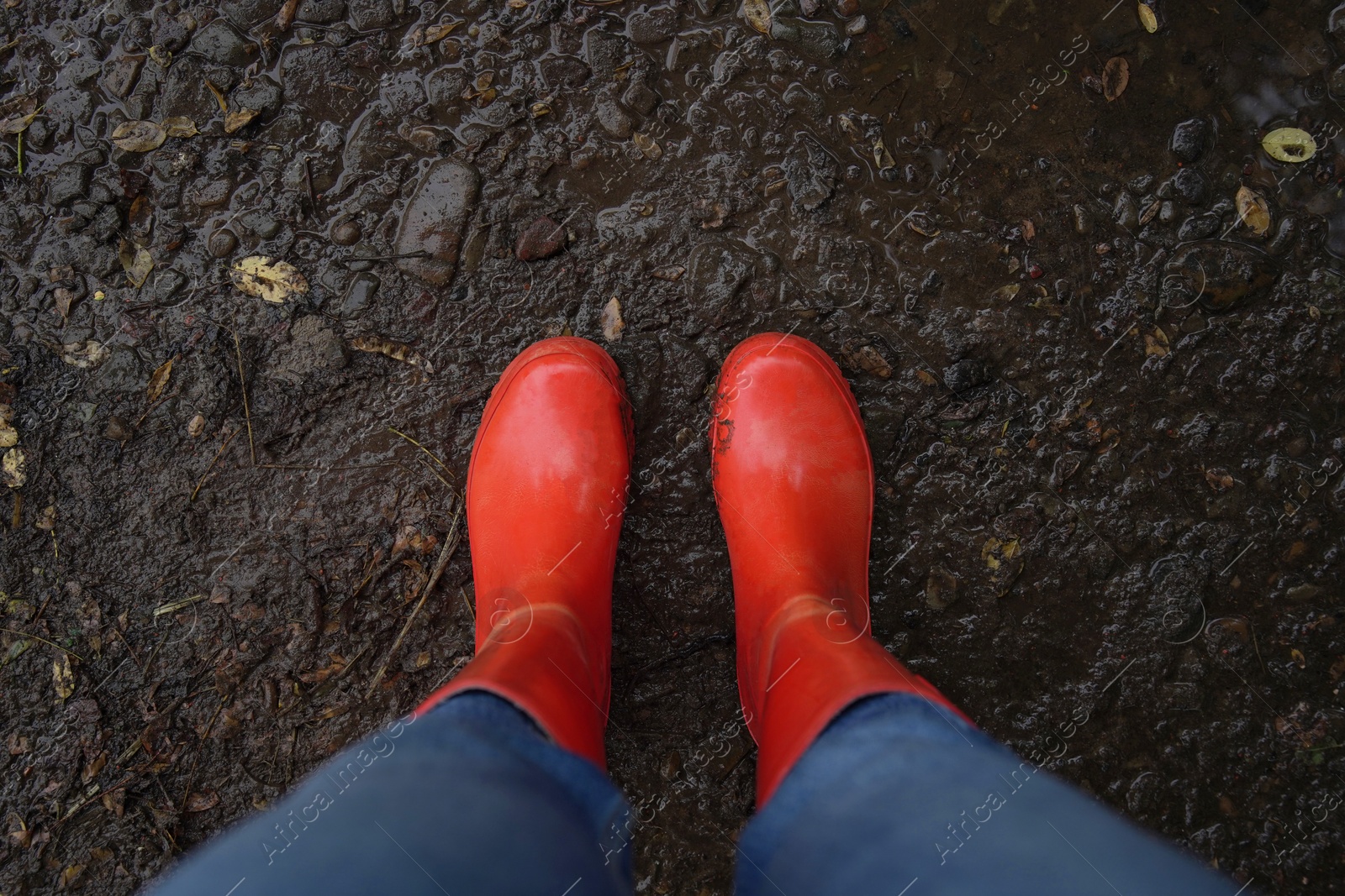 Photo of Woman wearing red rubber boots standing on muddy road, top view