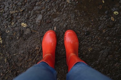 Woman wearing red rubber boots standing on muddy road, top view