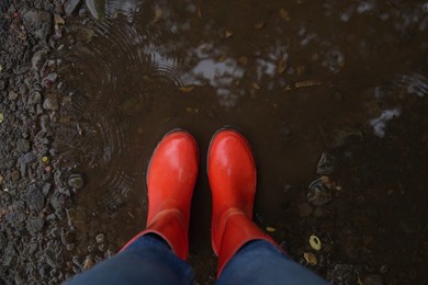 Woman wearing red rubber boots standing in rippled puddle, top view