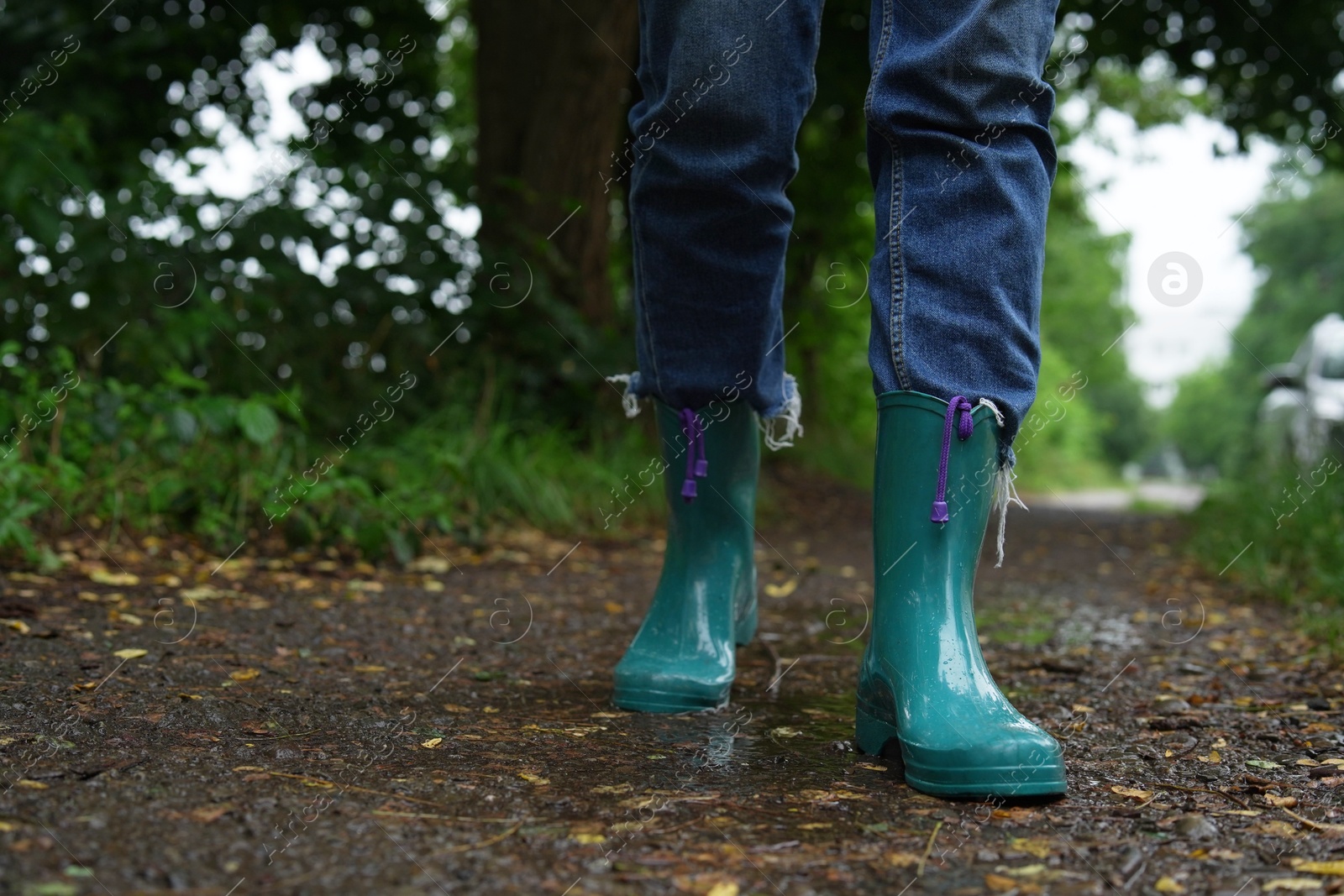 Photo of Woman in turquoise rubber boots walking on wet road, closeup. Space for text