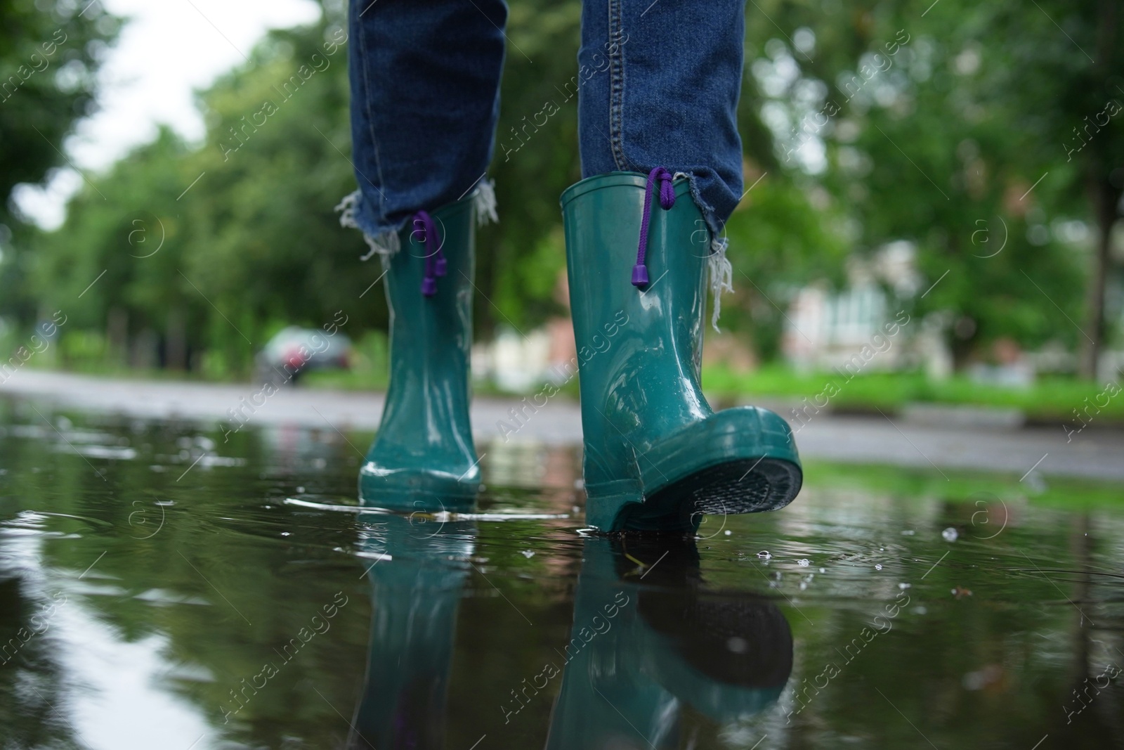 Photo of Woman wearing turquoise rubber boots walking in puddle outdoors, closeup