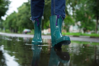 Woman wearing turquoise rubber boots walking in puddle outdoors, closeup