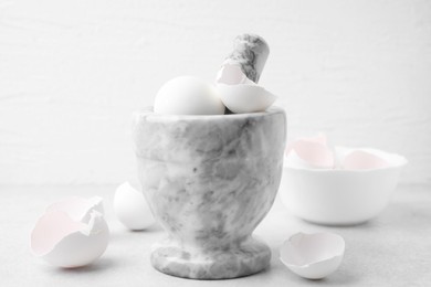 Photo of Broken eggshells, mortar and pestle on grey table, closeup