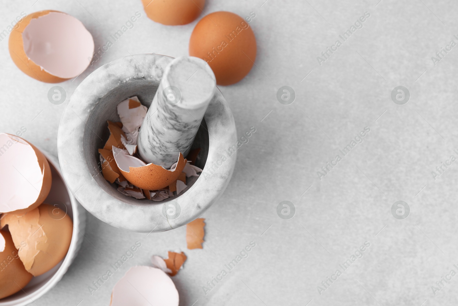 Photo of Broken eggshells, mortar and pestle on grey table, flat lay. Space for text