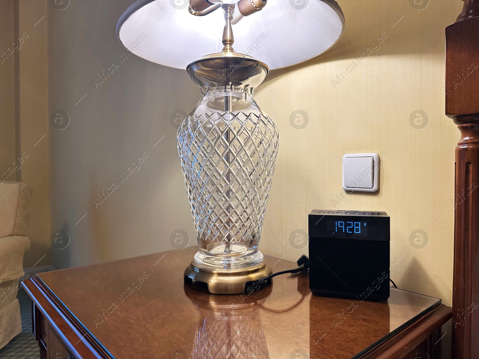 Photo of Lamp and electric clock on wooden bedside in luxury hotel