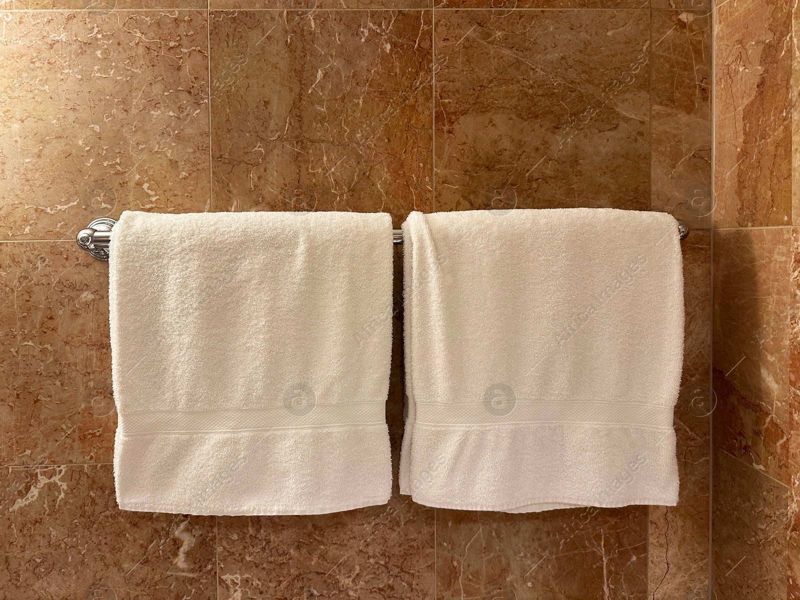 Photo of Soft terry towels hanging on tiled wall in hotel bathroom