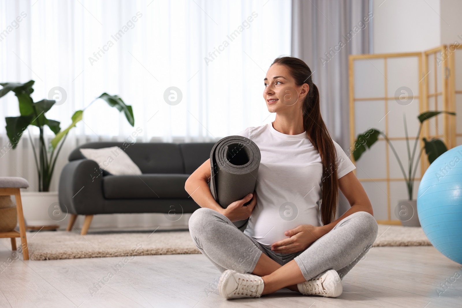 Photo of Pregnant woman with exercise mat on floor at home