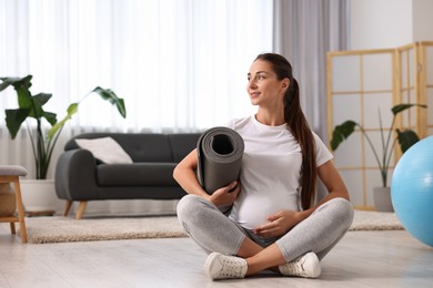 Photo of Pregnant woman with exercise mat on floor at home