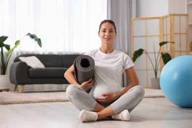 Smiling pregnant woman with exercise mat on floor at home