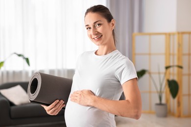 Photo of Smiling pregnant woman with exercise mat at home