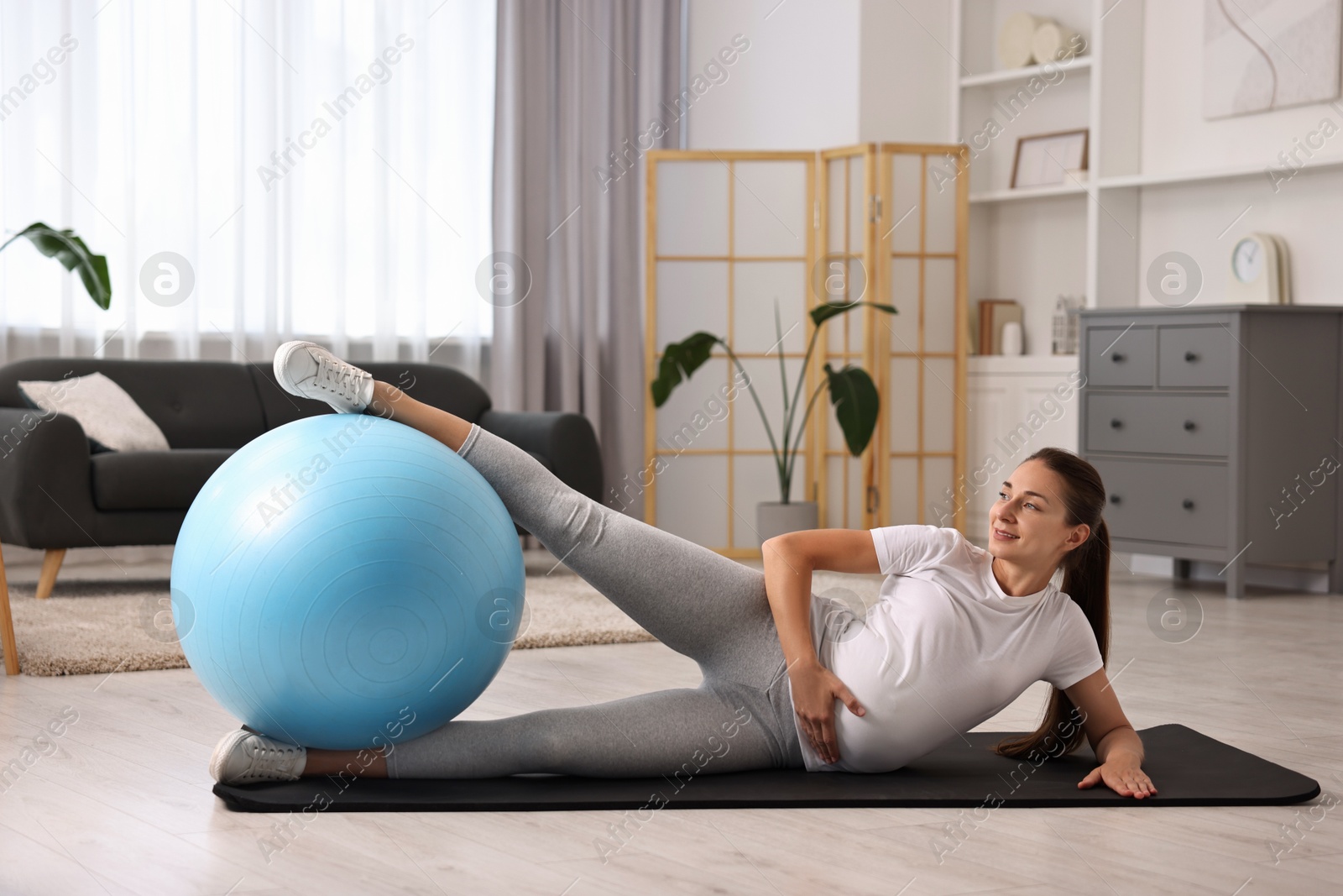 Photo of Beautiful pregnant woman doing exercises with fitball on mat at home