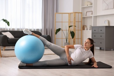 Beautiful pregnant woman doing exercises with fitball on mat at home