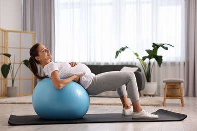 Beautiful pregnant woman doing exercises on fitball at home