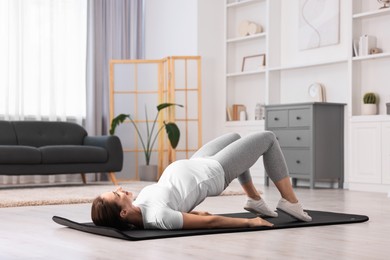 Beautiful pregnant woman doing stretching exercises on mat at home