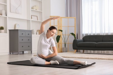 Beautiful pregnant woman doing stretching exercises on mat at home