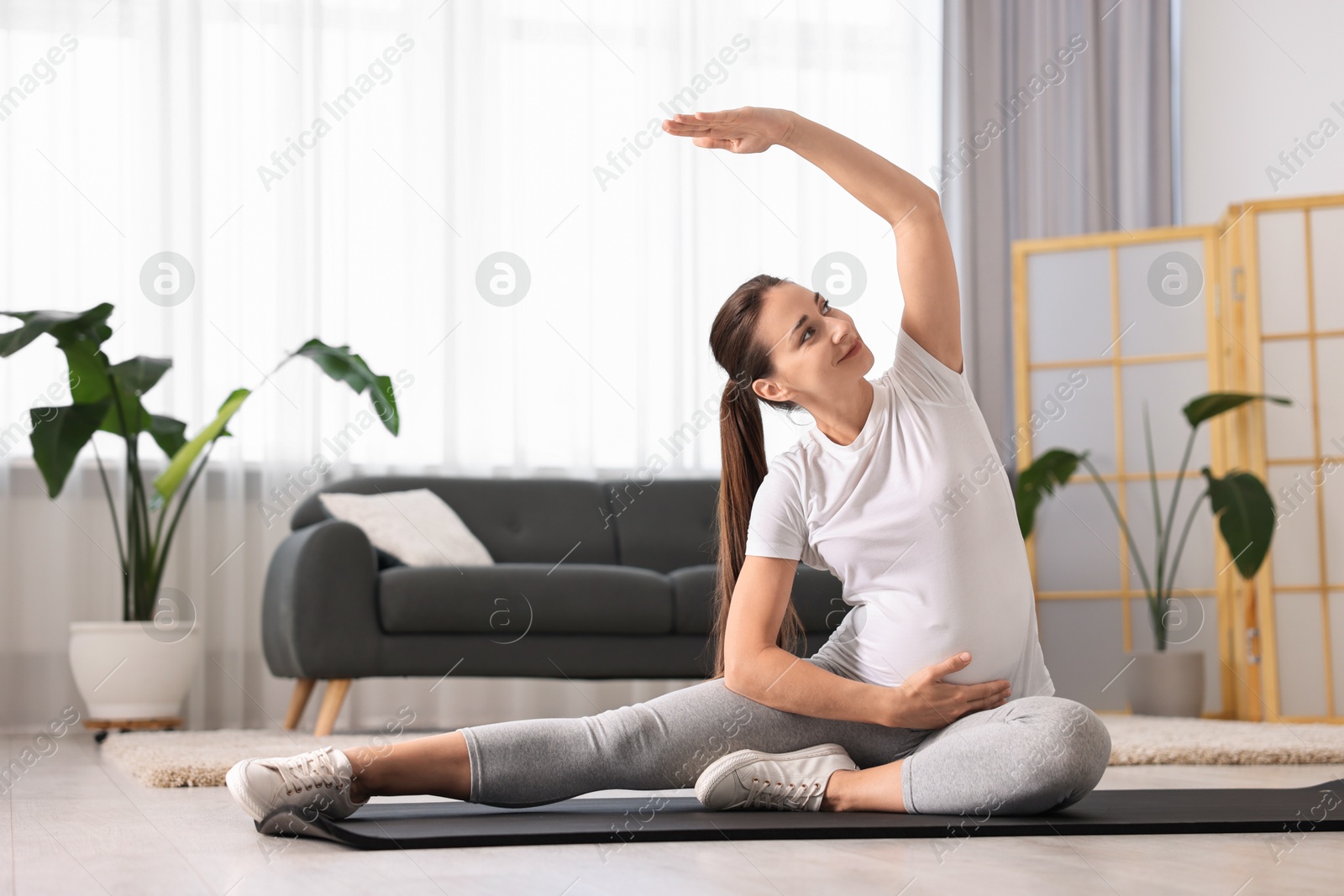 Photo of Beautiful pregnant woman doing stretching exercises on mat at home