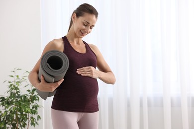 Photo of Beautiful pregnant woman with exercise mat at home, space for text