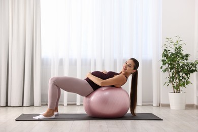 Beautiful pregnant woman doing exercises on fitball at home