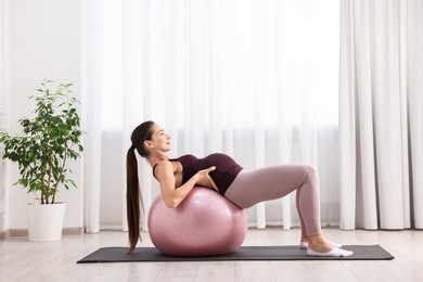 Beautiful pregnant woman doing exercises on fitball at home