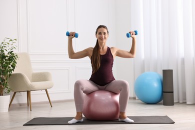 Beautiful pregnant woman with dumbbells doing exercises on fitball at home