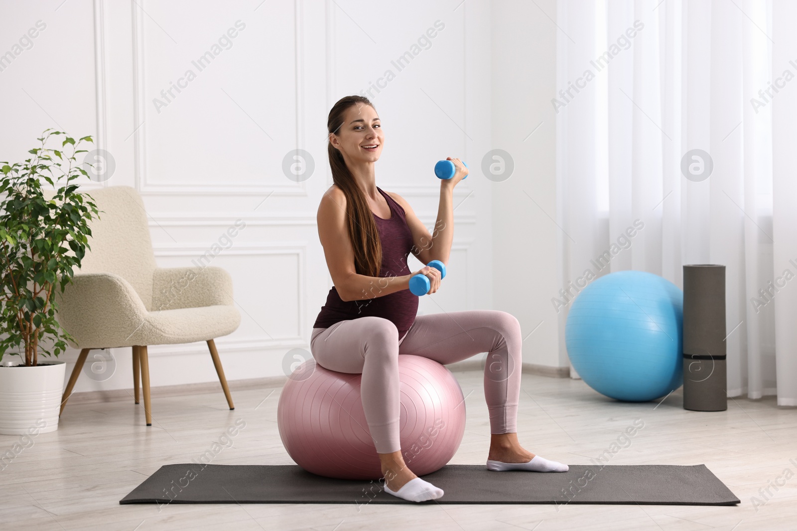 Photo of Beautiful pregnant woman with dumbbells doing exercises on fitball at home