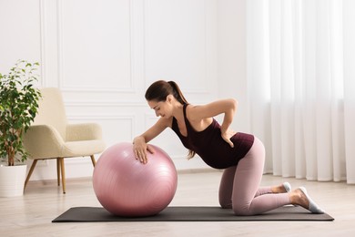 Photo of Beautiful pregnant woman doing exercises with fitball on mat at home