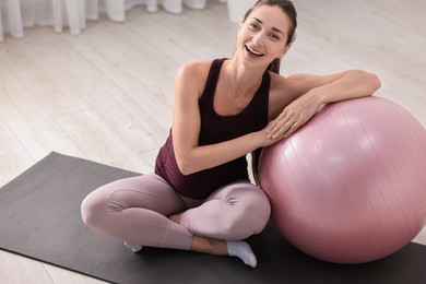 Beautiful pregnant woman with fitball on exercise mat at home