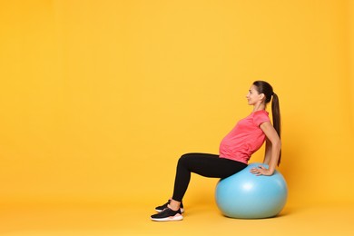 Beautiful pregnant woman doing exercises on fitball against yellow background