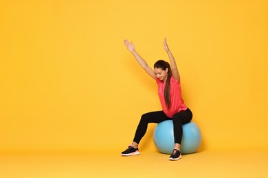 Photo of Beautiful pregnant woman doing exercises on fitball against yellow background, space for text