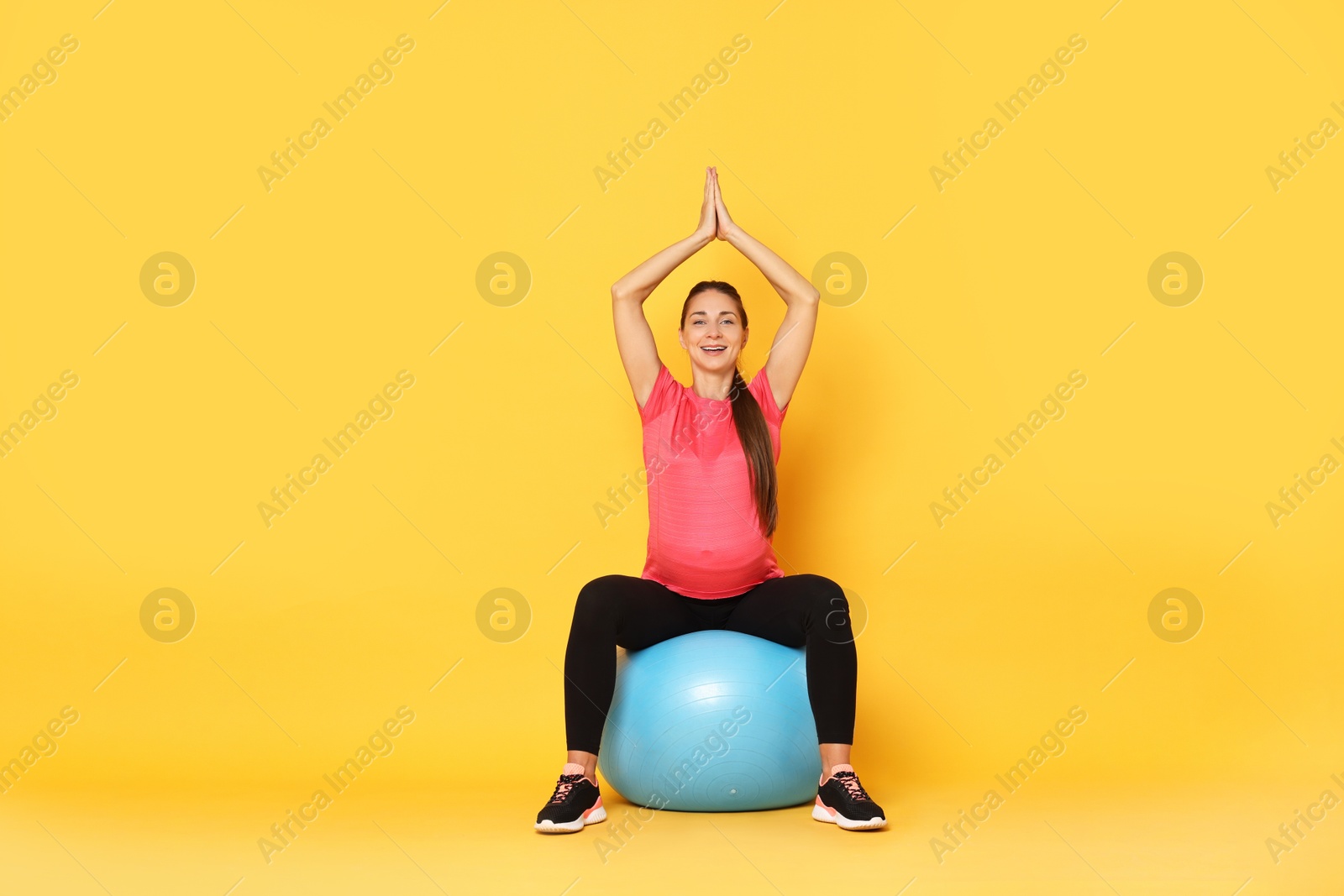 Photo of Beautiful pregnant woman doing exercises on fitball against yellow background