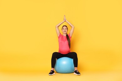 Photo of Beautiful pregnant woman doing exercises on fitball against yellow background