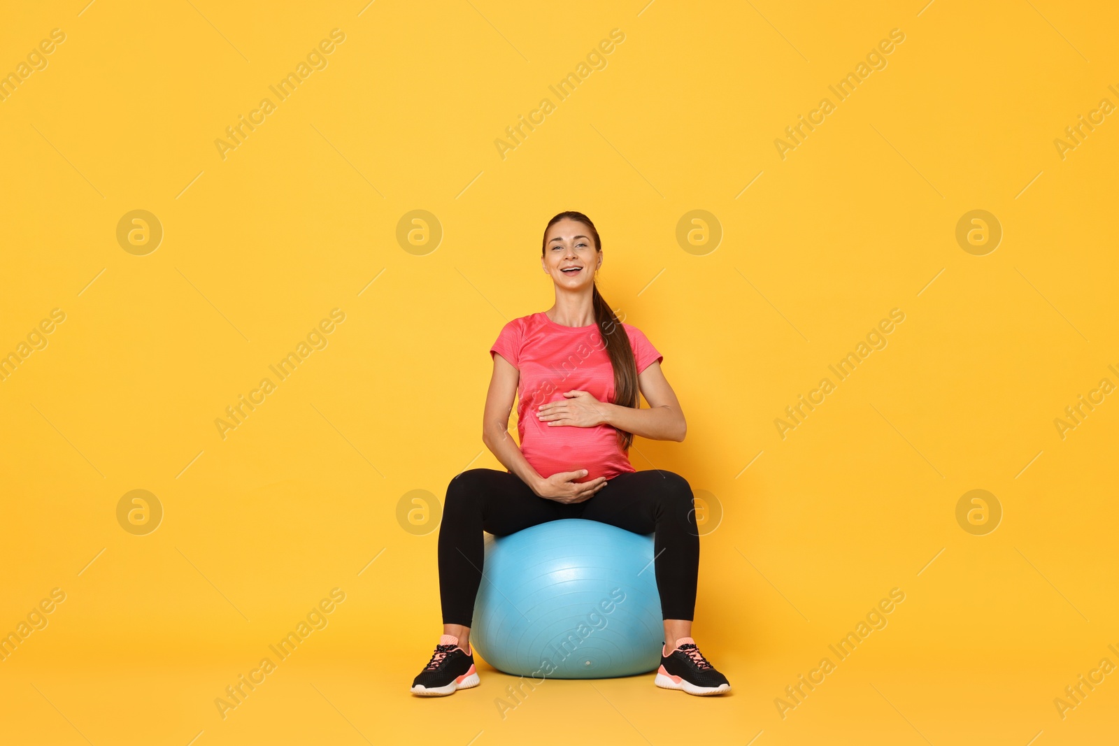 Photo of Beautiful pregnant woman doing exercises on fitball against yellow background