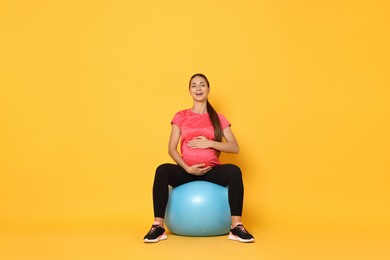 Beautiful pregnant woman doing exercises on fitball against yellow background