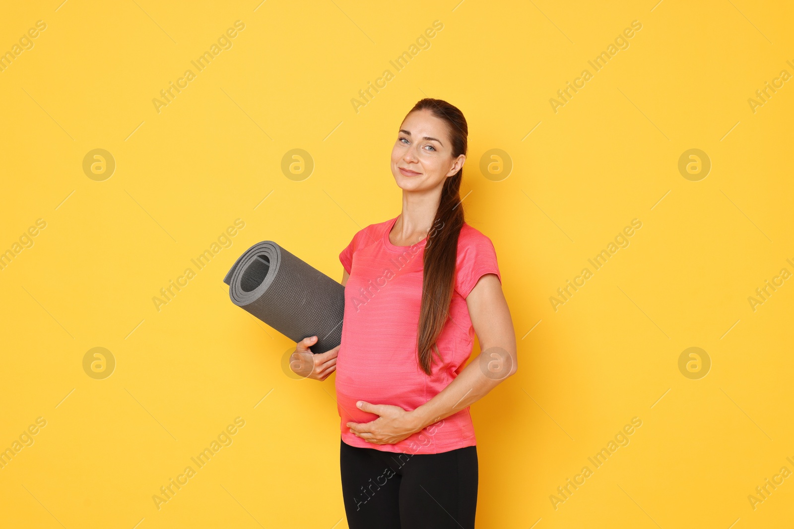 Photo of Beautiful pregnant woman with exercise mat on yellow background