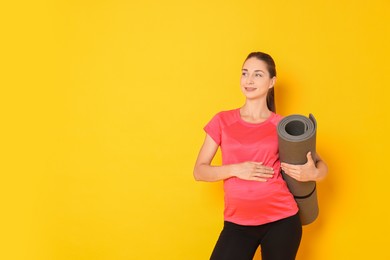 Photo of Beautiful pregnant woman with exercise mat on yellow background, space for text