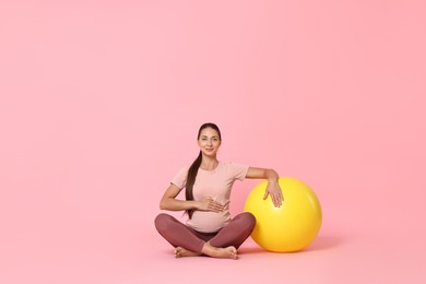 Photo of Beautiful pregnant woman with fitball on pink background