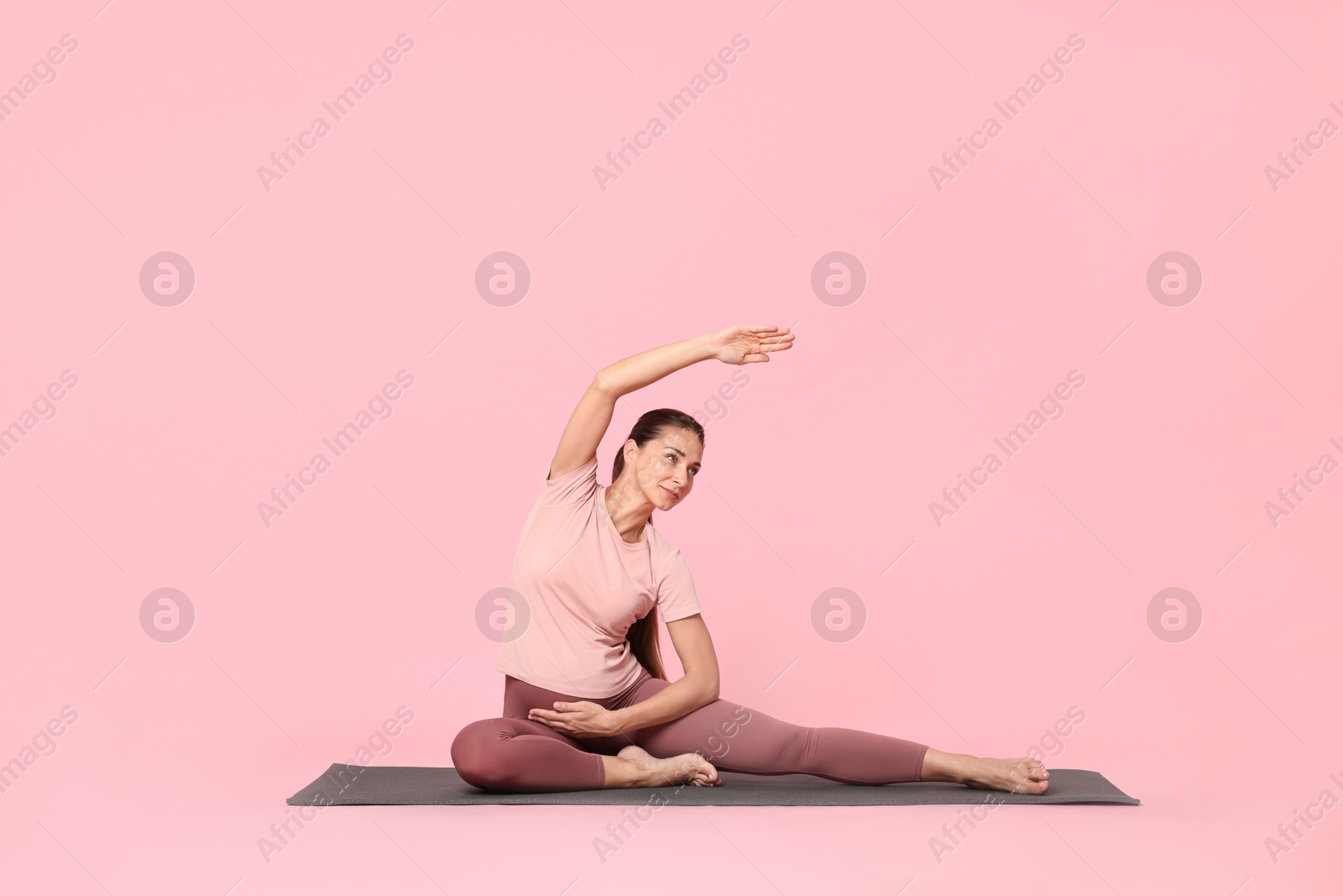 Photo of Beautiful pregnant woman doing stretching exercises on mat against pink background