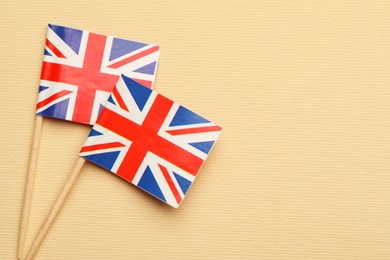 Small paper flags of United Kingdom on beige background, top view. Space for text