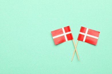 Small paper flags of Denmark on turquoise background, top view. Space for text