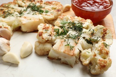 Photo of Delicious grilled cauliflower steaks with sauce and garlic on grey table, closeup