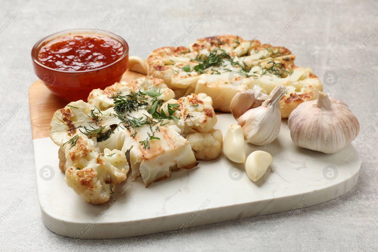 Photo of Delicious grilled cauliflower steaks with sauce and garlic on grey table, closeup