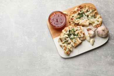 Photo of Delicious grilled cauliflower steaks with sauce and garlic on grey table, above view. Space for text