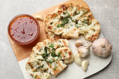 Photo of Delicious grilled cauliflower steaks with sauce and garlic on grey table, above view